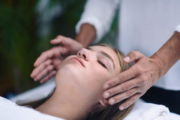 Reiki therapist holding hands on both sides of patient head and transfer energy. Beautiful and peaceful teenage girl lying with her eyes closed. Alternative therapy concept.